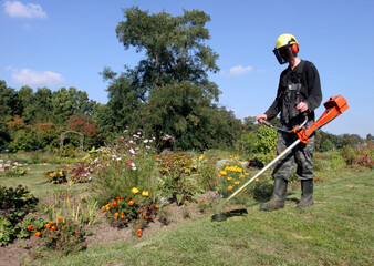 Gardener using a string trimmer to maintain flower beds in a vibrant garden on a sunny day