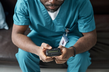 Healthcare worker in blue scrubs analyzing data on handheld device while sitting on couch. Focused and precise, engaging with technology for vital information © pressmaster