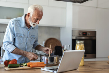 Happy senior man having fun cooking at home. Elderly person preparing health lunch in modern...
