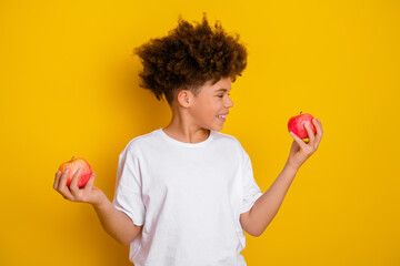 Young boy holding apples in both hands against a bright yellow background, expressing cheerful...