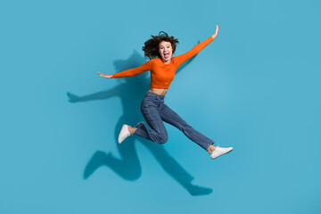 Joyful young woman in stylish casual outfit jumping against vibrant blue background showcasing...