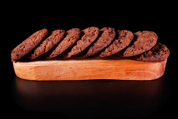 Sweet chocolate chip cookies are arranged in rows on wood and placed on a black surface and...