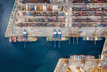 Aerial top down view of a large container cargo ship terminal with industrial vessels being loaded and unloaded