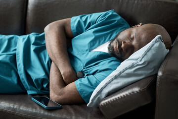 Medical professional sleeping on a sofa in scrubs after a long shift resting head on a pillow....