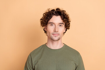 Fototapeta premium Portrait of a young curly-haired man in a green khaki shirt against a muted beige background expressing calm style
