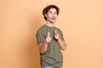 Young man in casual khaki t-shirt gesturing enthusiastically with both hands against beige...