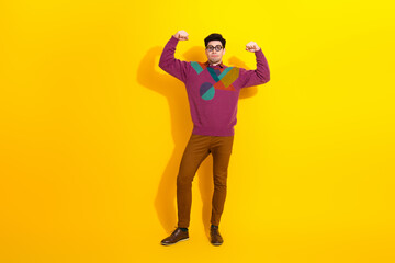 Confident young man in vibrant attire making a power pose against a yellow background, expressing energy and stylish confidence