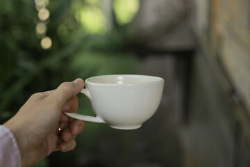 Male Hand Holding White Cup with Blurred Natural Background