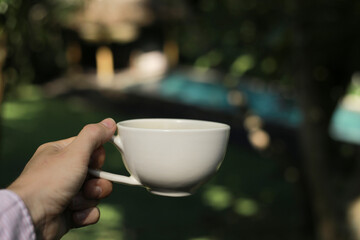 Male Hand Holding White Cup with Blurred Natural Background