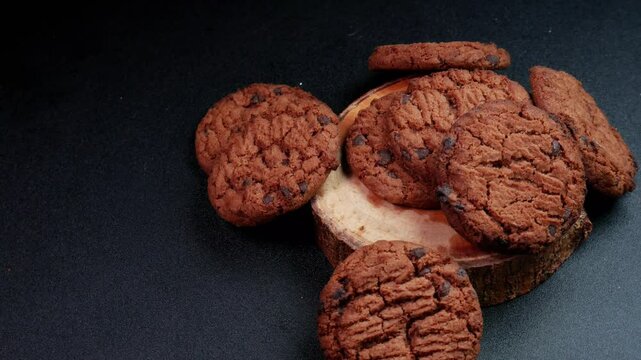Top view rotating motion of stack of crispy sweet chocolate cookies on wood with dark background. Perfect for advertising or promotion of food products.