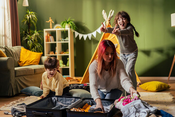 Mother packing suitcase with playful children in living room
