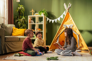Girl reading a story to her younger brothers in a teepee tent