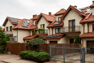Modern townhouses line a street, featuring tiled roofs and balconies. Rooftop solar panels on multiple homes highlight sustainable living and community wide renewable energy adoption.