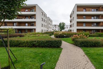 A winding paved path meanders through spacious common areas of a modern European residential quarter. Lawns and hedges line the walkway, linking apartments and promoting community.