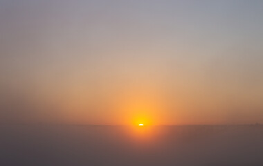 The rising sun on the horizon, thick fog colored by sunlight