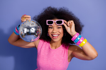 Young woman in stylish pink outfit holding disco ball in hand with a cheerful expression and trendy...