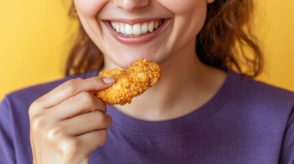 Joyful Woman Enjoys a Crispy Chicken Tender: A Delicious Bite of Fried Goodness on a Sunny Yellow Backdrop, Perfect for Foodies