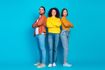 Fototapeta premium Three diverse young friends confidently pose together in casual outfits against a vibrant blue background, embodying unity and friendship