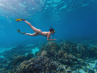 A woman swims gracefully underwater, discovering colorful coral reefs and marine life. Bright...