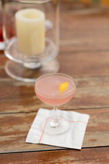 cold refreshing cosmopolitan cocktail in a coupe glass sitting on outdoor table at event cocktail hour