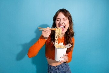 Happy young woman enjoying noodles from a takeaway box using chopsticks in a colorful and stylish...