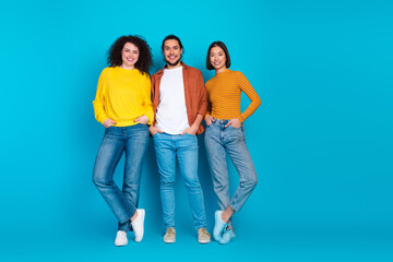 Obraz premium Young diverse friends bonding together posing in stylish casual outfits on a bright blue background, promoting friendship