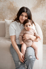 baby and mother, mom hugging baby at home, maternal love and care, mom with a small child, brown or beige background