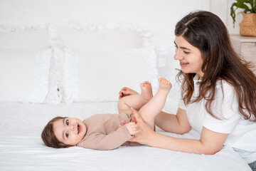baby and mother, mom kissing baby's feet on a white bed at home, maternal love and care, mom with a small child at home