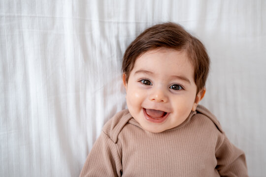 a baby, a close-up portrait of a smiling or laughing baby boy on a white bed, a place for text