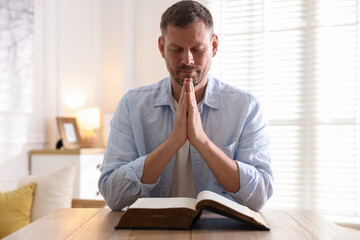 Man with Bible praying at table indoors