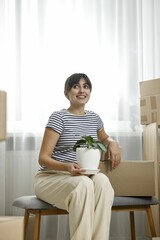 Moving day. Happy woman with houseplant and cardboard boxes in her new home
