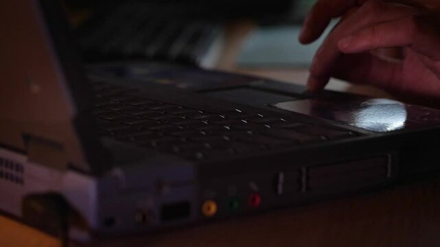 Close-up of hands actively typing on a laptop keyboard in a dimly lit environment, suggesting focused work, coding, or late-night activity