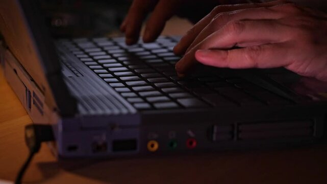 Close-up of hands actively typing on a laptop keyboard in a dimly lit environment, suggesting focused work, coding, or late-night activity