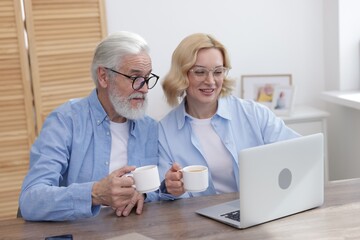 Fototapeta premium Senior man and mature woman with coffee watching something on laptop at home. Happy couple