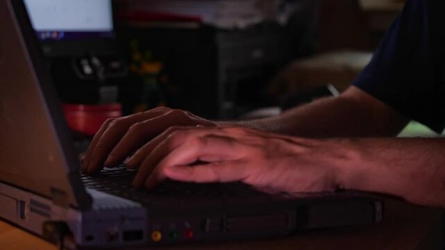 Close-up of hands actively typing on a laptop keyboard in a dimly lit environment, suggesting focused work, coding, or late-night activity