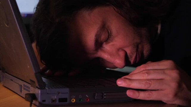 A close-up shot captures the weary mood of an exhausted person with long hair, face down on a laptop keyboard, illuminated by a warm glow, suggesting late-night work or profound fatigue