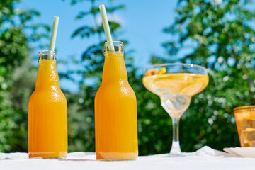 Cold summer drink. Refreshing fresh orange juice in bottles with drinking straw on the table in the garden.