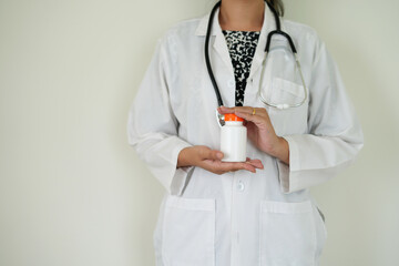 An asian young doctor with stethoscope is holding an medicine bottle to assess the quality of medicine, recommending medication  to patient and explaining the dose and description of the medication.