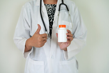 An asian young doctor with stethoscope is holding an medicine bottle to assess the quality of...