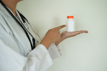 An asian young doctor with stethoscope is holding an medicine bottle to assess the quality of...