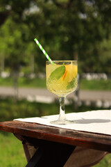 Lemonade on a blurred nature background. Close-up of a glass with a cocktail outdoors. Lemonade or other drink in a glass. Summer refreshing drink with mint and orange slices