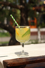 Lemonade on a blurred nature background. Close-up of a glass with a cocktail outdoors. Lemonade or other drink in a glass. Summer refreshing drink with mint and orange slices