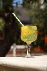 Lemonade on a blurred nature background. Close-up of a glass with a cocktail outdoors. Lemonade or other drink in a glass. Summer refreshing drink with mint and orange slices