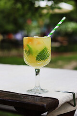 Lemonade on a blurred nature background. Close-up of a glass with a cocktail outdoors. Lemonade or other drink in a glass. Summer refreshing drink with mint and orange slices