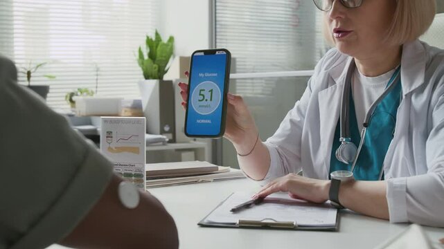 Confident female clinician scanning glucose monitor sensor on male patient arm with smartphone, then showing him data on gadget screen and giving medical advice