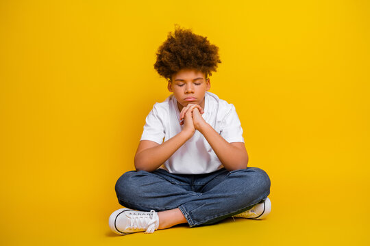 Thoughtful teenage boy sitting on the floor against yellow background, showcasing modern casual fashion and deep contemplation