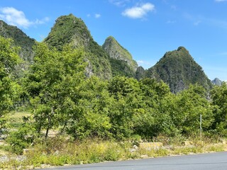 A stunning vista unfolds, displaying verdant mountains, trees, and clear skies under sunlight in Guangxi, China.