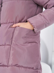 Person wearing a mauve puffer jacket with hand in side pocket. The quilted texture is visible, highlighting the stitching patterns. The sleeve also has a cuffed design, adding warmth
