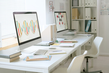 Workstation in modern lab showing computer screens with scientific patterns and research books on desk. Clean and organized lab environment without people