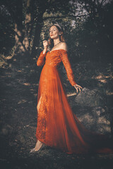 Fototapeta premium Pretty woman in red apparel making rituals in dark forest